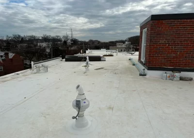 Flat, white rooftop under a cloudy sky with vents, pipes, and a brick structure on the right side.