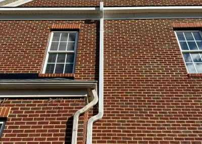 White gutter pipes run along a brick house exterior with two windows and a garage door.