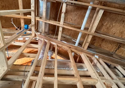 View of exposed wooden framing, ducts, pipes, and wiring inside a house under construction.