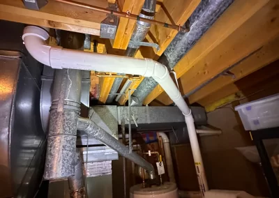 Basement ceiling with exposed pipes, ducts, and water heater beneath wooden beams, shot with flash.