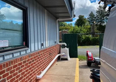 Sidewalk beside a brick building, with a white utility van and equipment under a partly cloudy sky.