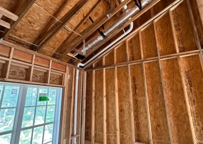 Room under construction with exposed wooden framing, insulation, wiring, and a window letting in sunlight.