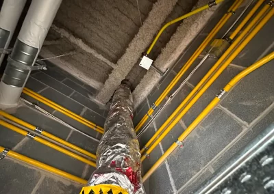 Insulated duct and yellow pipes run along a concrete wall and ceiling in an industrial or mechanical space.