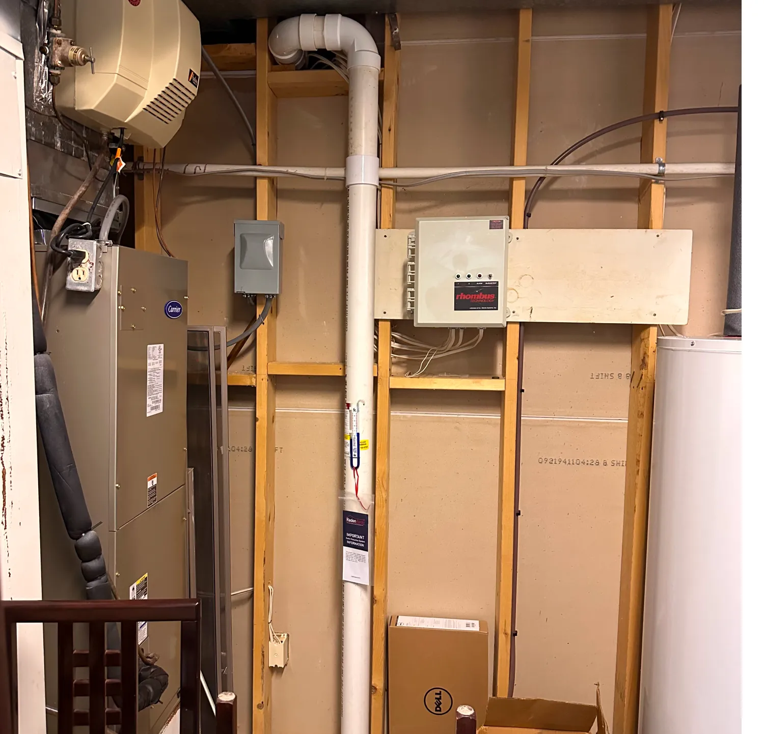 Furnace, water heater, pipes, and electrical panel in an unfinished basement utility room with exposed walls.